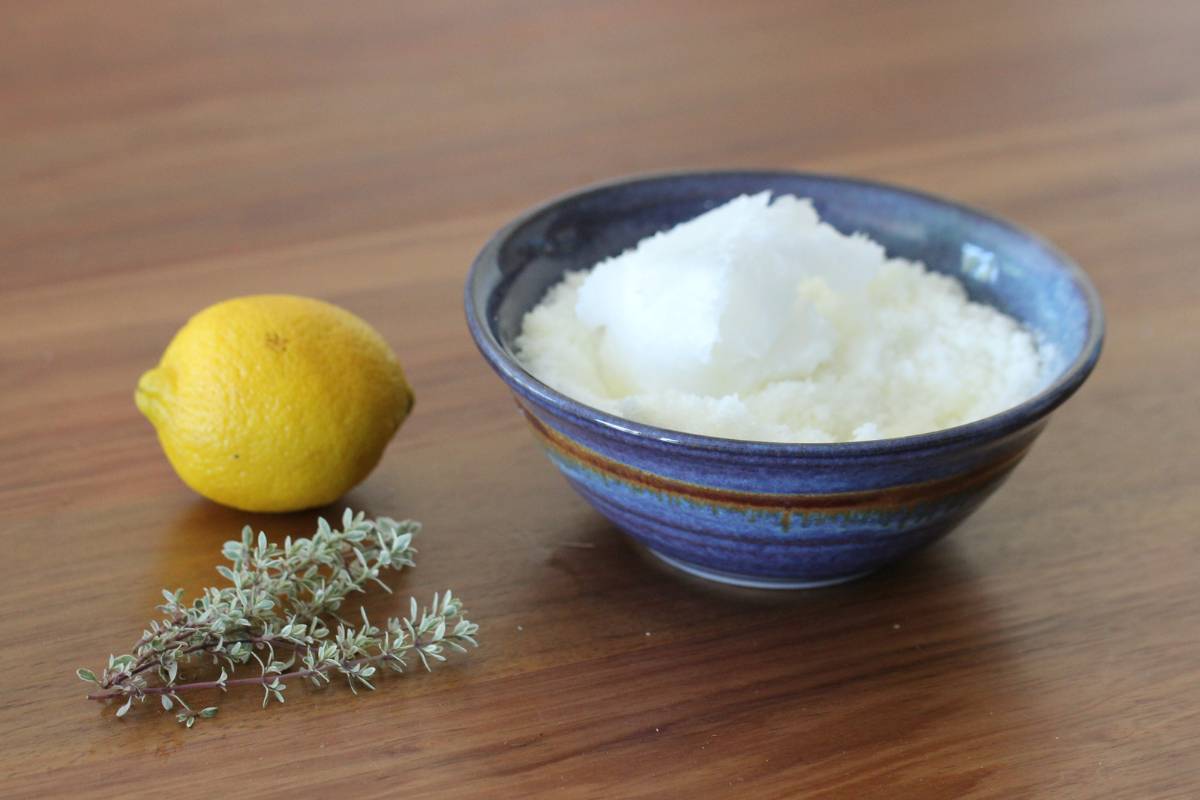 A bowl containing salt, olive oil and coconut oil sitting next to a lemon and some thyme sprigs