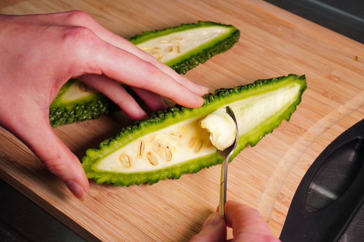 A person using a spoon to scoop the seeds from the middle of a bitter melon fruit