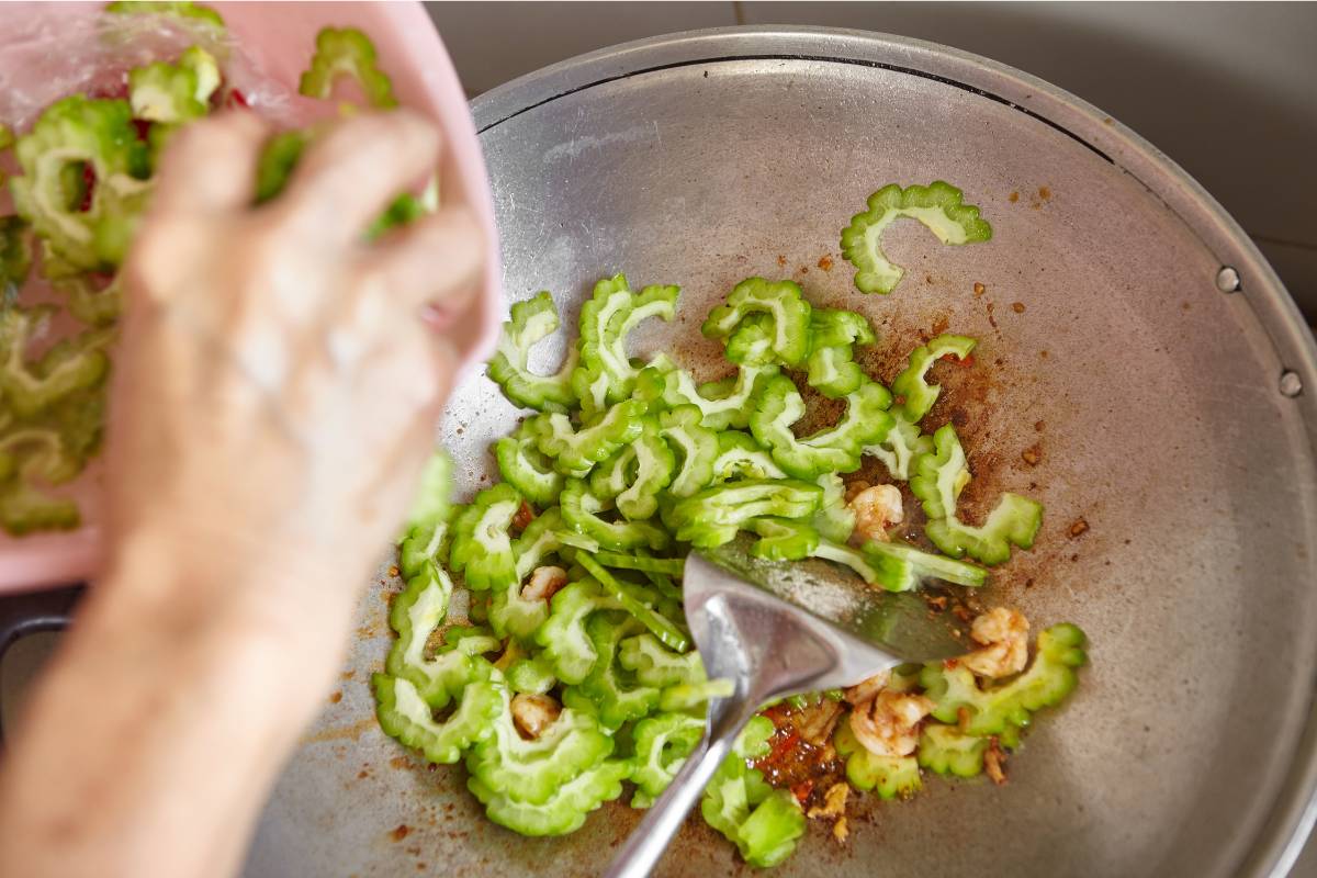 A photo of a cook wok frying slices of bitter melon. The fruit has been soaked and blanched in an ice bath before cooking.