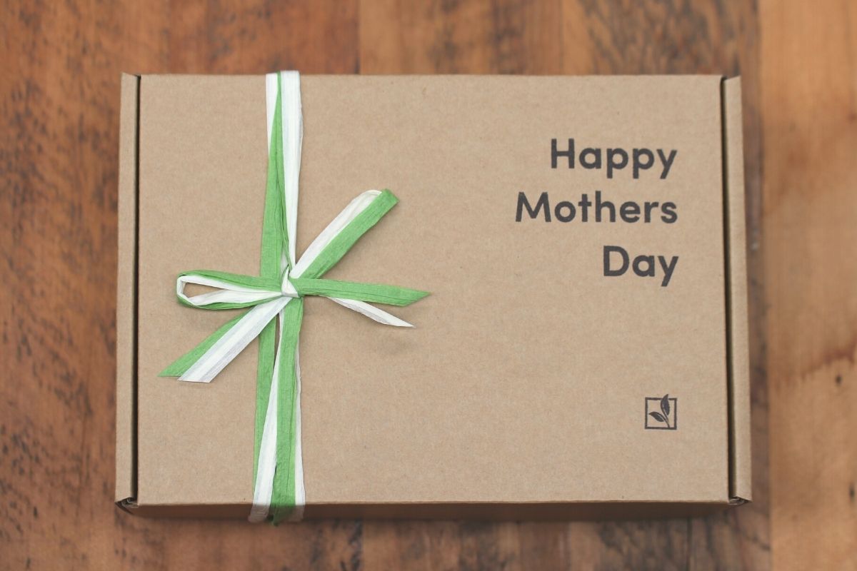 A cardboard gift box saying 'Happy Mothers Day' with green and white paper ribbon.