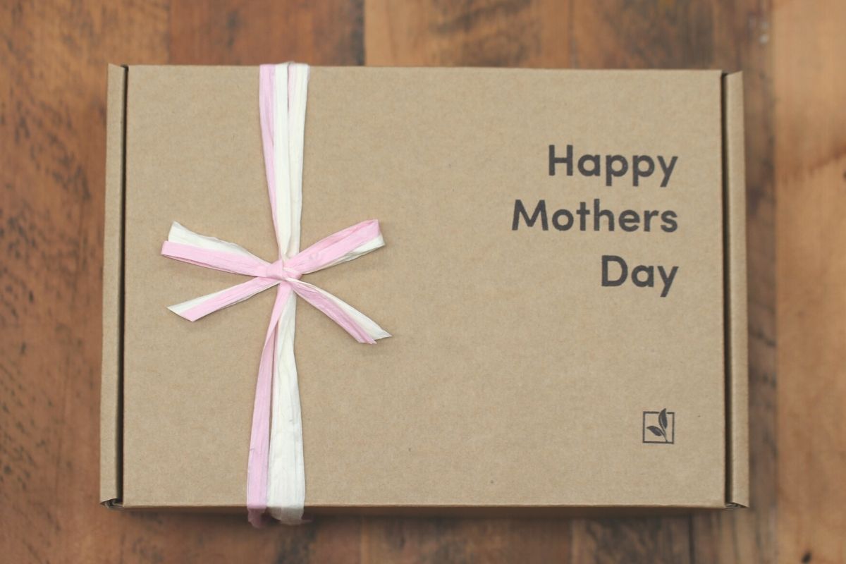 A cardboard gift box saying 'Happy Mothers Day' with a pink and white paper ribbon.