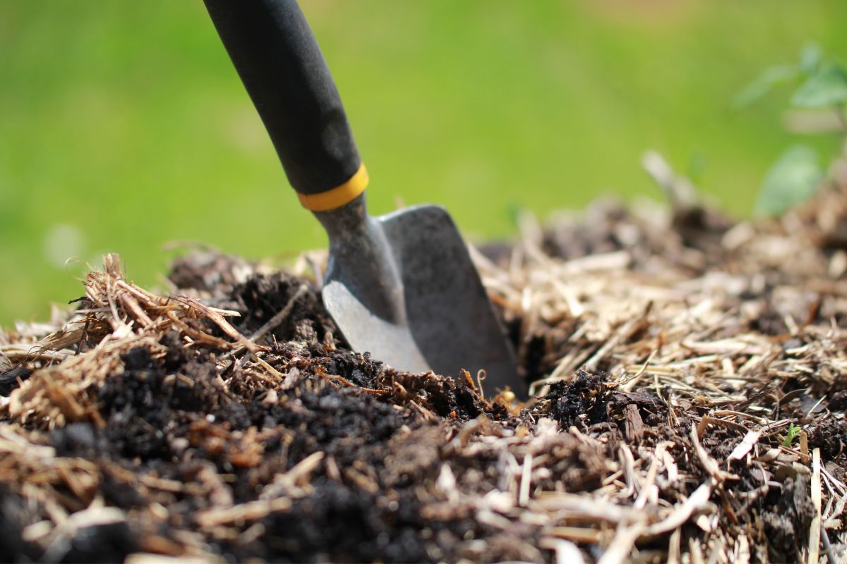 A sturdy trowel being used to dig a planting hole in the top of a straw bale